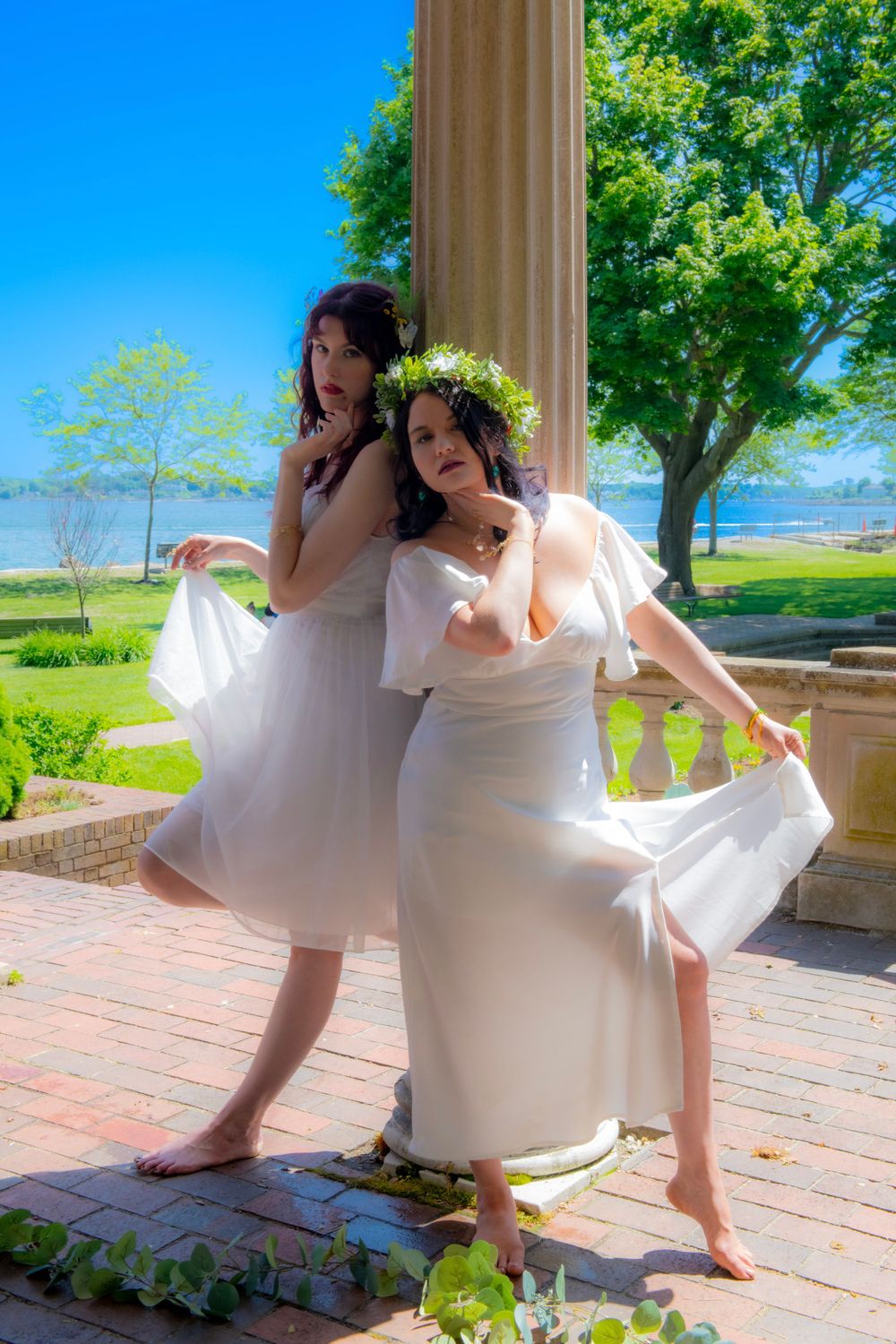 Women in ethereal white dresses dancing barefoot on a brick terrace with columns and greenery.
