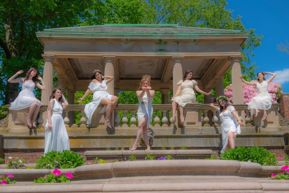 Group performing choreographed dance movements on outdoor stone stage with columns.