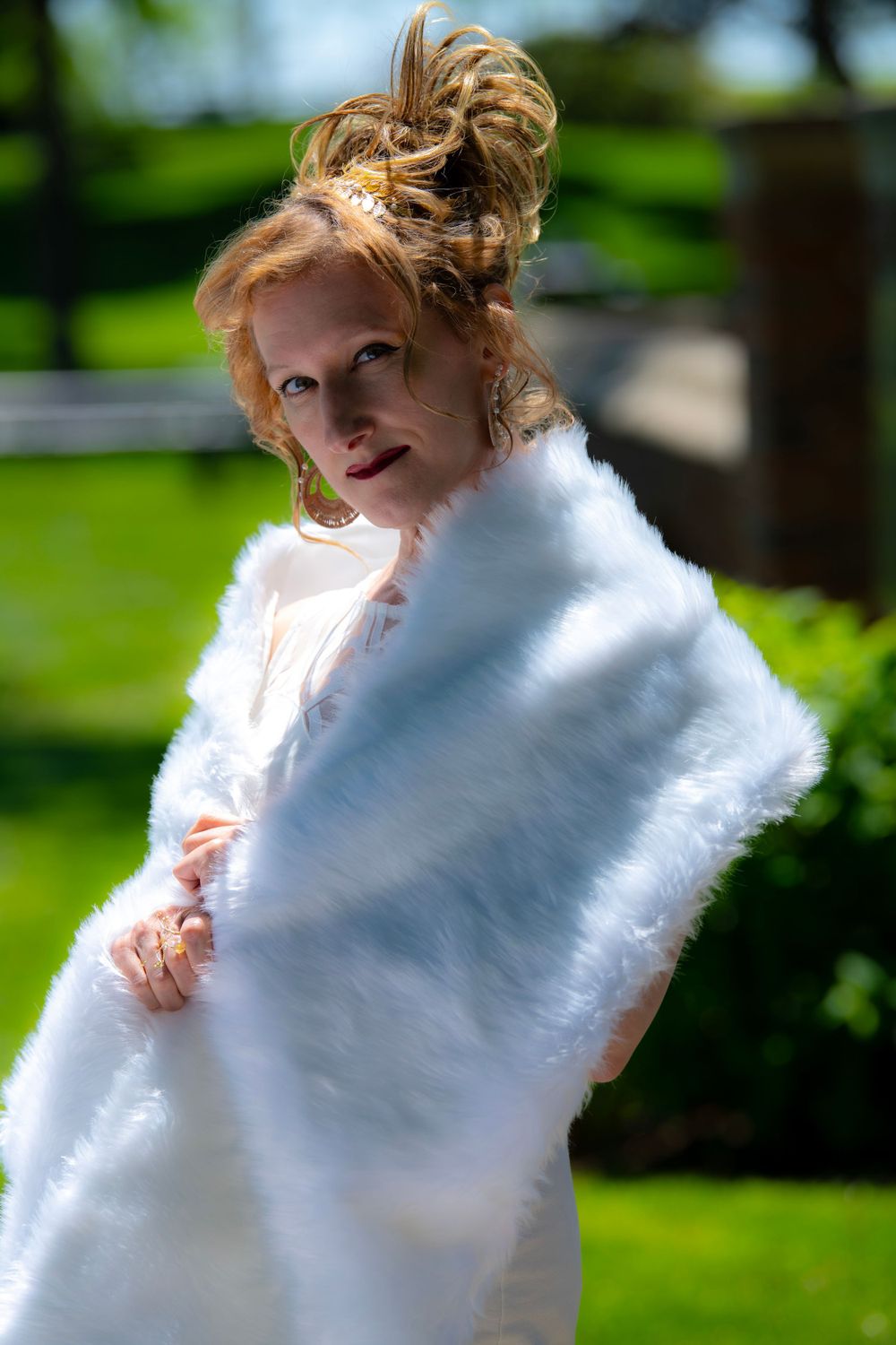 Portrait in bright sunlight featuring white fur wrap and elegant updo hairstyle.