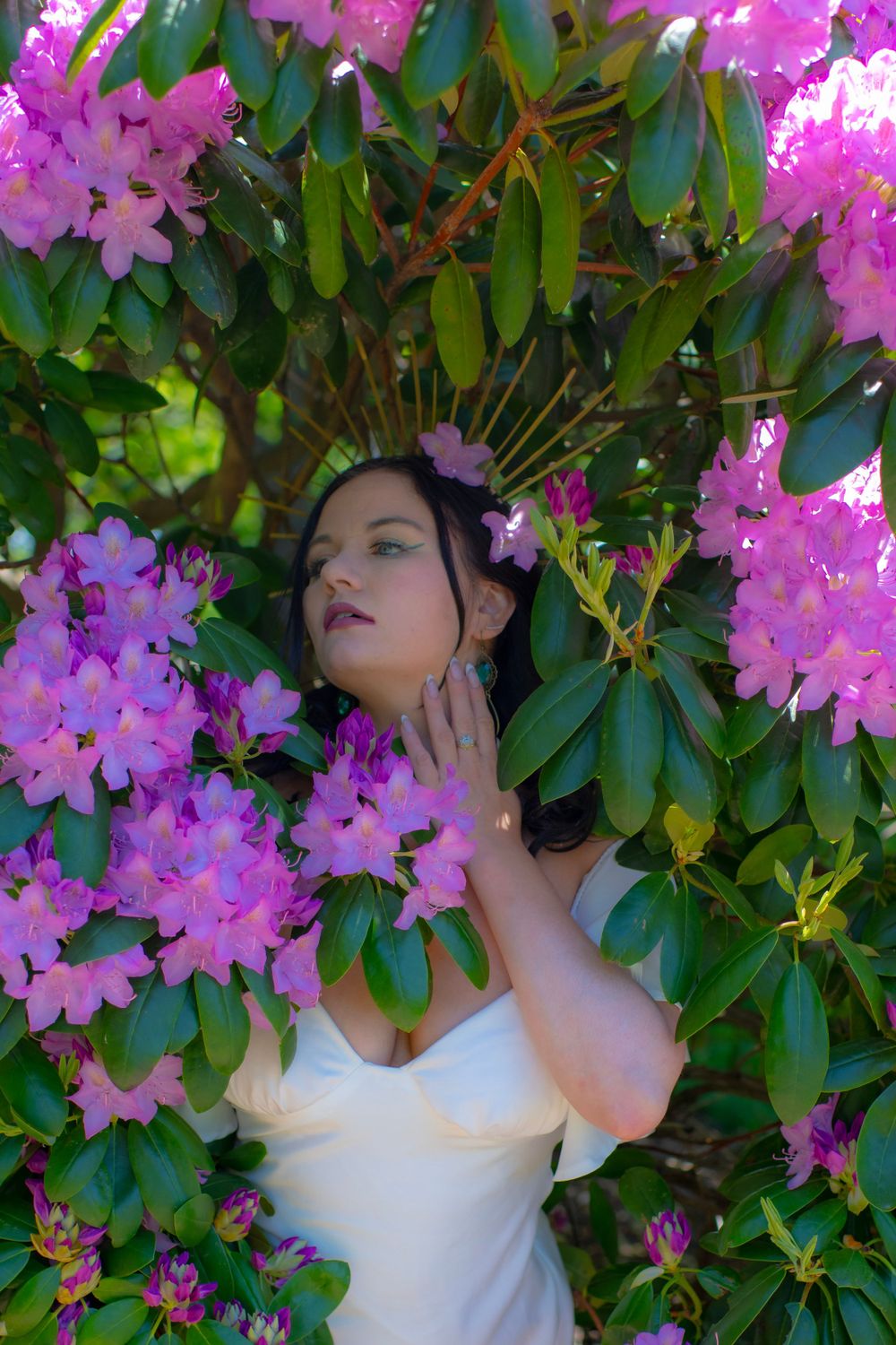 Romantic portrait amidst vibrant pink rhododendron blooms in a white dress.
