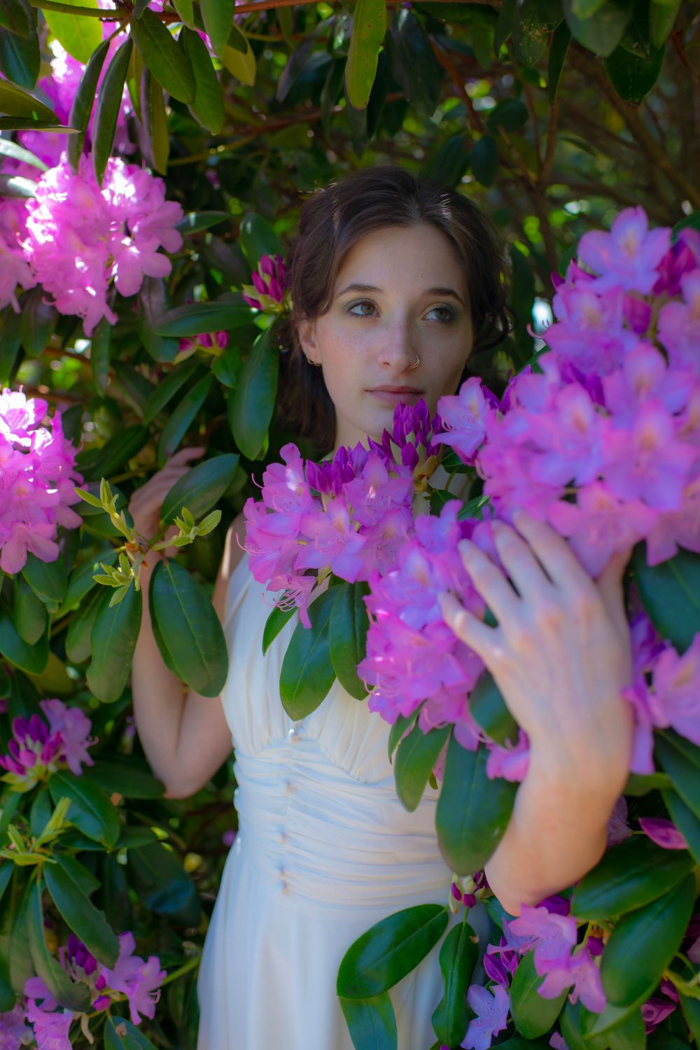Artistic portrait surrounded by blooming pink rhododendrons and lush green leaves.