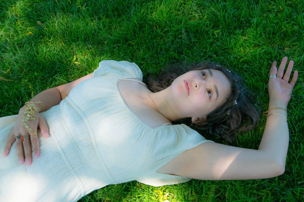 A person in a white dress lays gracefully on sunlit grass during an outdoor photoshoot.