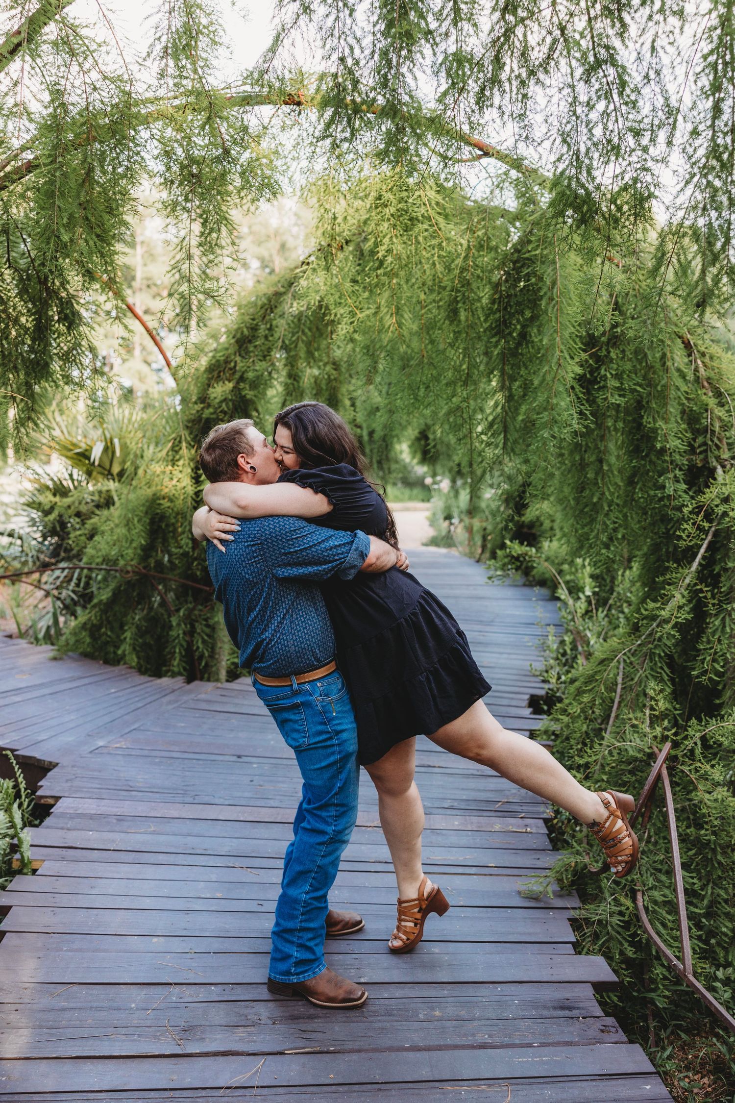 Romantic couple dancing on wooden boardwalk surrounded by willow trees.