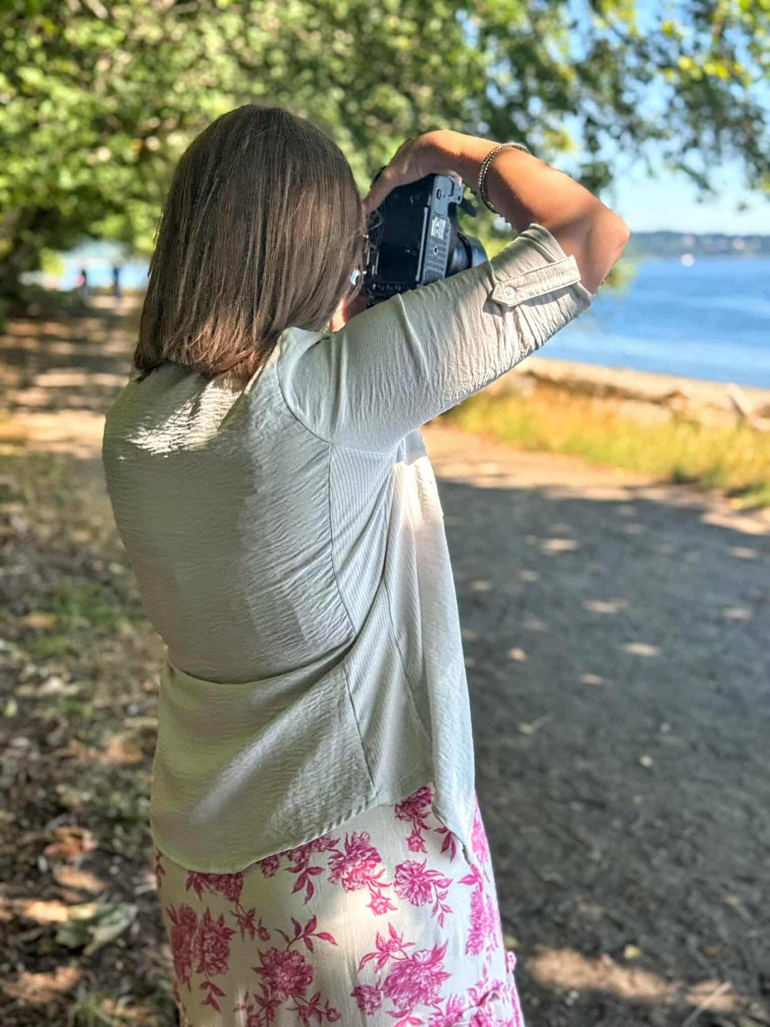 Photographer taking pictures near a waterfront path with trees and lake in background.