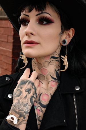 Dramatic portrait showcasing bone earrings, neck tattoos and leather jacket against red brick wall.