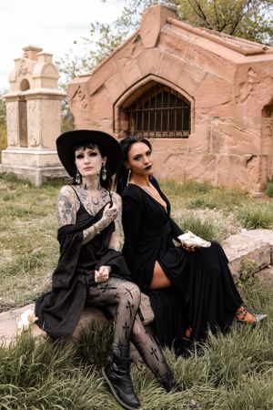 Gothic fashion photoshoot featuring two models in black outfits near stone architecture.