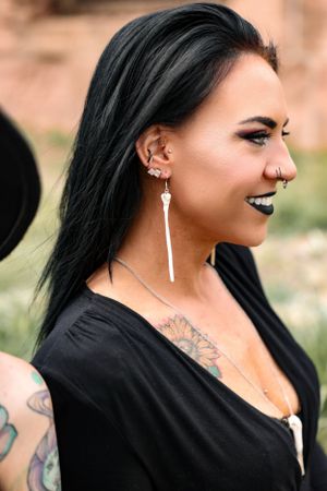 Portrait featuring bone earring jewelry and nose piercing with natural smile against outdoor backdrop.