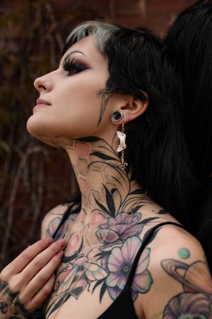 Close-up portrait showcasing intricate floral neck tattoos and detailed eye makeup in dark aesthetic style.