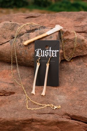 Bone shaped jewelry pieces with gold chain displayed on red rock surface with Luster brand card.