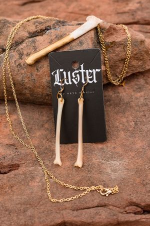 Bone-shaped jewelry and gothic brand card displayed on red rock surface with gold chain.