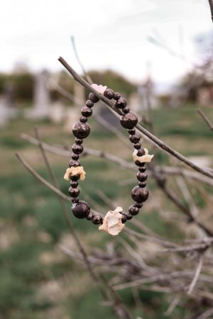 Dark and light beaded bracelet with skull accent displayed on bare tree branches.