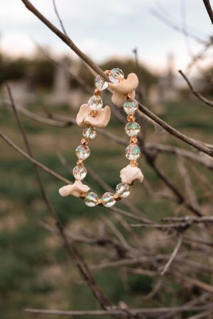 Crystal and bone-colored beaded bracelet displayed on tree branches with soft bokeh background.
