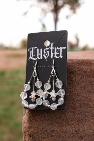 Crystal beaded chandelier earrings on a black Luster branded display card against stone background.