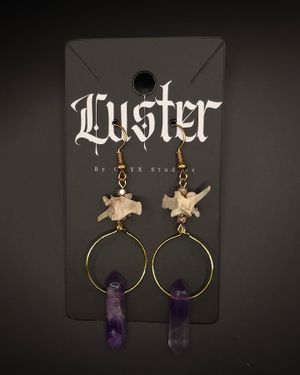 Alternative earrings with vertebrae and purple crystal points hanging from brass hoops on dark display.