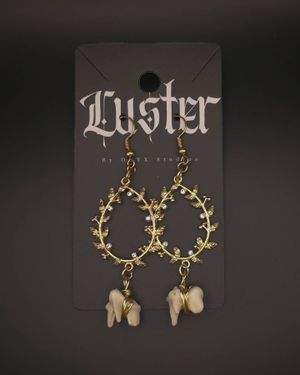 Ornate brass circle earrings with thorny detail and small bone charms on black display card.