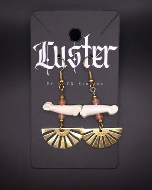 Boho style earrings with bone fragments and brass fan-shaped pendants on black display.