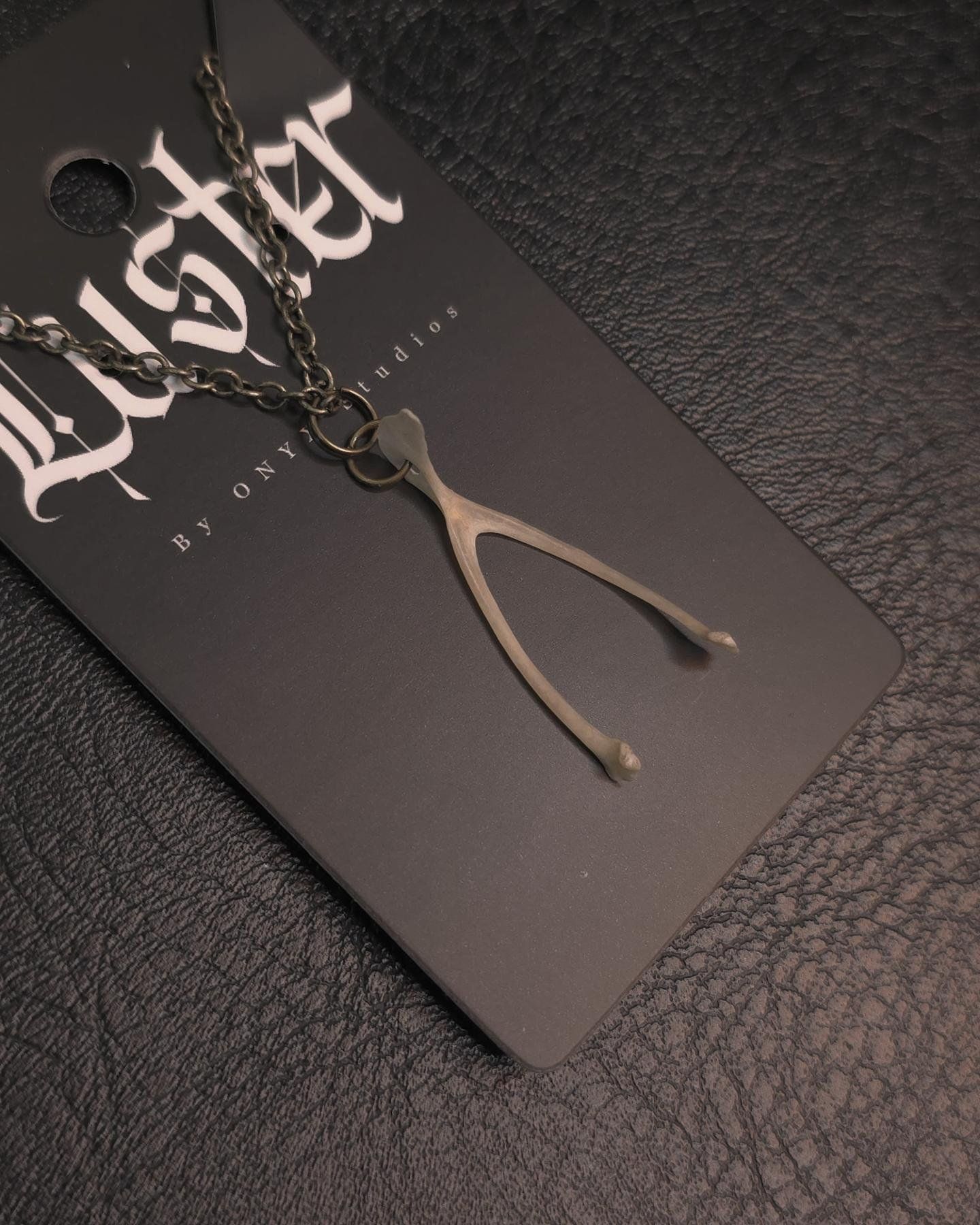 Close-up of antique brass wishbone pendant necklace on dark textured background.