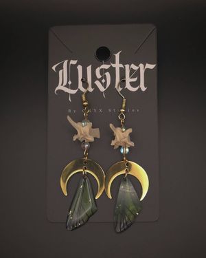 Gothic jewelry display featuring dark green butterfly wing earrings with brass crescent moons on black card.