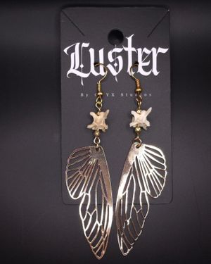 Ethereal metallic butterfly wing earrings with bone accents on gothic brand display.