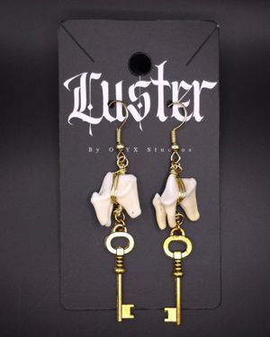 Vintage-style brass key earrings with bone accents displayed on gothic branded card.