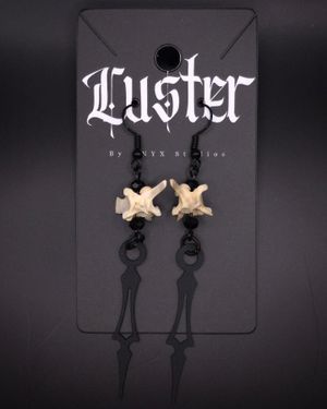 Gothic bone and black metal dangle earrings displayed on dark branded card.