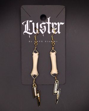 Bone-shaped earrings with lightning bolt charms displayed on dark jewelry card.