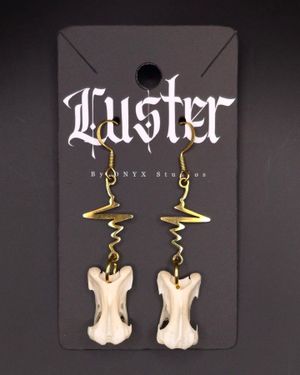 Gold spiral wire earrings with hanging bone pendants displayed on dark branded card.