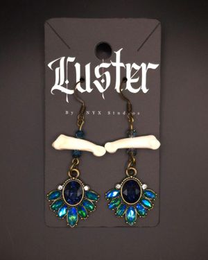 Gothic jewelry featuring bone-shaped pendants with blue gemstone drops displayed on a black Luster branded card.