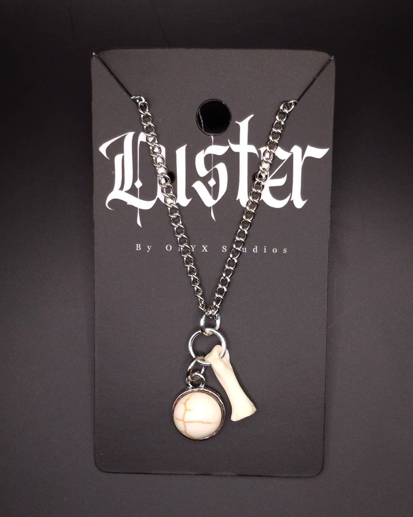 Vintage-inspired chain necklace with bone charm and timepiece pendant on dark display card.