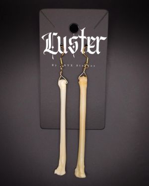 Long bone-shaped dangle earrings displayed on black Luster branded jewelry card.