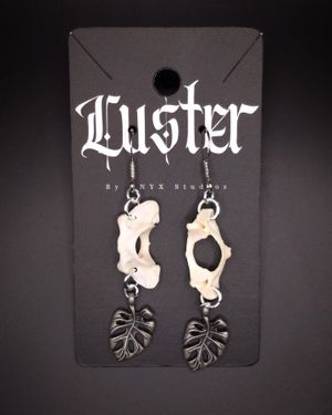 Gothic earrings featuring curved bone pieces with black monstera leaf charms on display card.