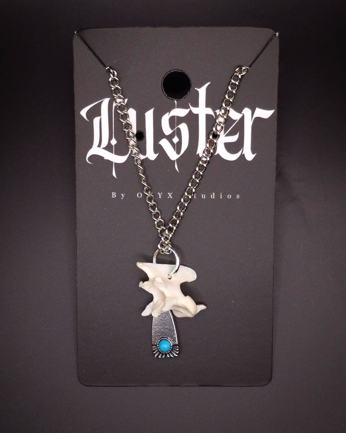 Gothic style necklace featuring bone fragments and turquoise stone on black display card.