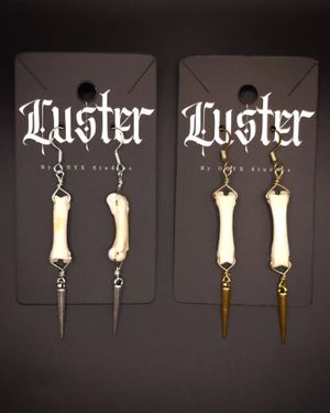 Two pairs of bone and spike pendant earrings on black branded display cards.