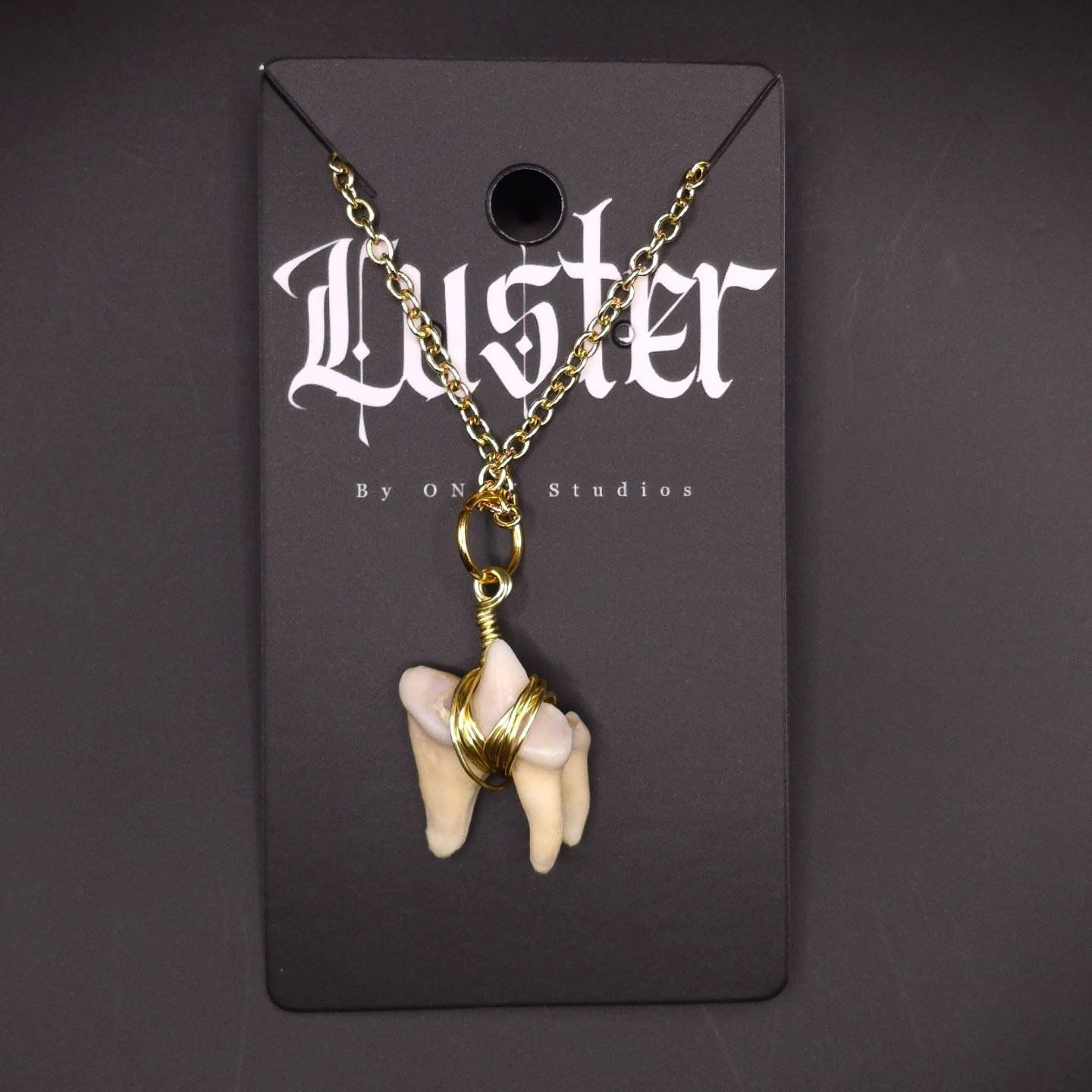Bone-inspired pendant necklace with gold chain displayed on dark gothic branding card.