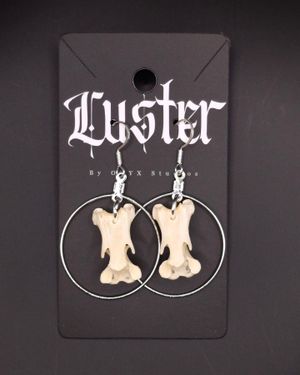 White bone pendants mounted within silver hoops displayed on a gothic-styled jewelry card.