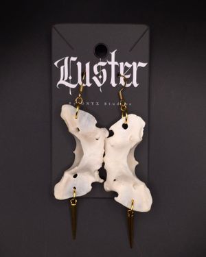 Dramatic white bone-inspired earrings with dangling spikes displayed on dark gothic branding card.