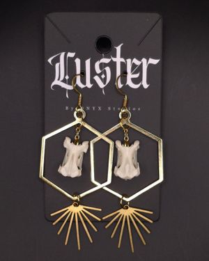 Gothic style hexagonal earrings with bone-like pendants and golden sunburst design on black display card.