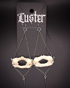 Gothic-style earrings featuring bone-shaped pendants hanging from dark metal chains against black display card.