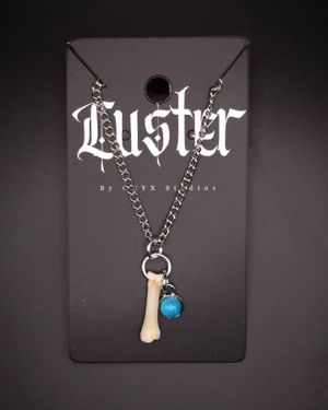 Silver chain necklace with bone pendant and blue stone charm displayed on gothic Luster branded card.