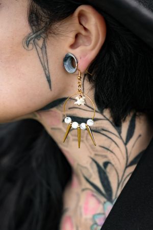 Detailed shot of a unique silver moon and spike statement earring with visible neck tattoos.