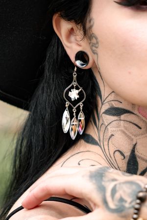 Close-up of ornate silver skull earring with dangling crystal elements.