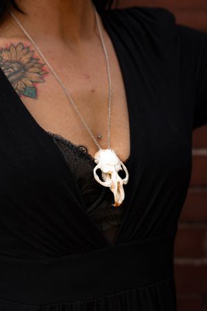 White skull pendant necklace worn with black lace top against brick wall.
