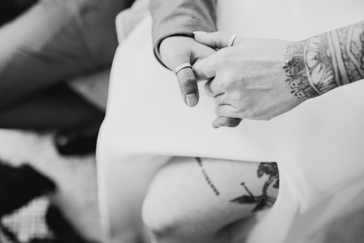 Black and white close-up photo of hands working on a tattoo, showing the tattoo machine and fresh ink on skin.