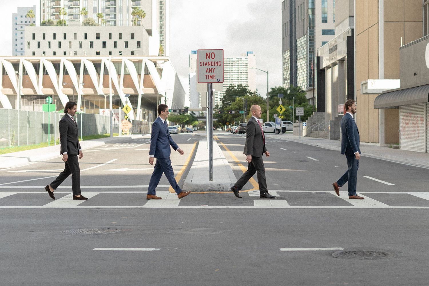 Four people recreate iconic Abbey Road crossing photo on modern city street.