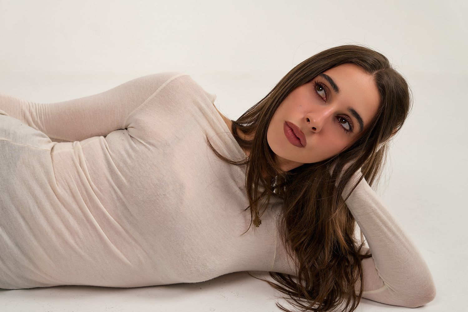 Young woman with brown hair lying down, wearing a white bodysuit against a white background.