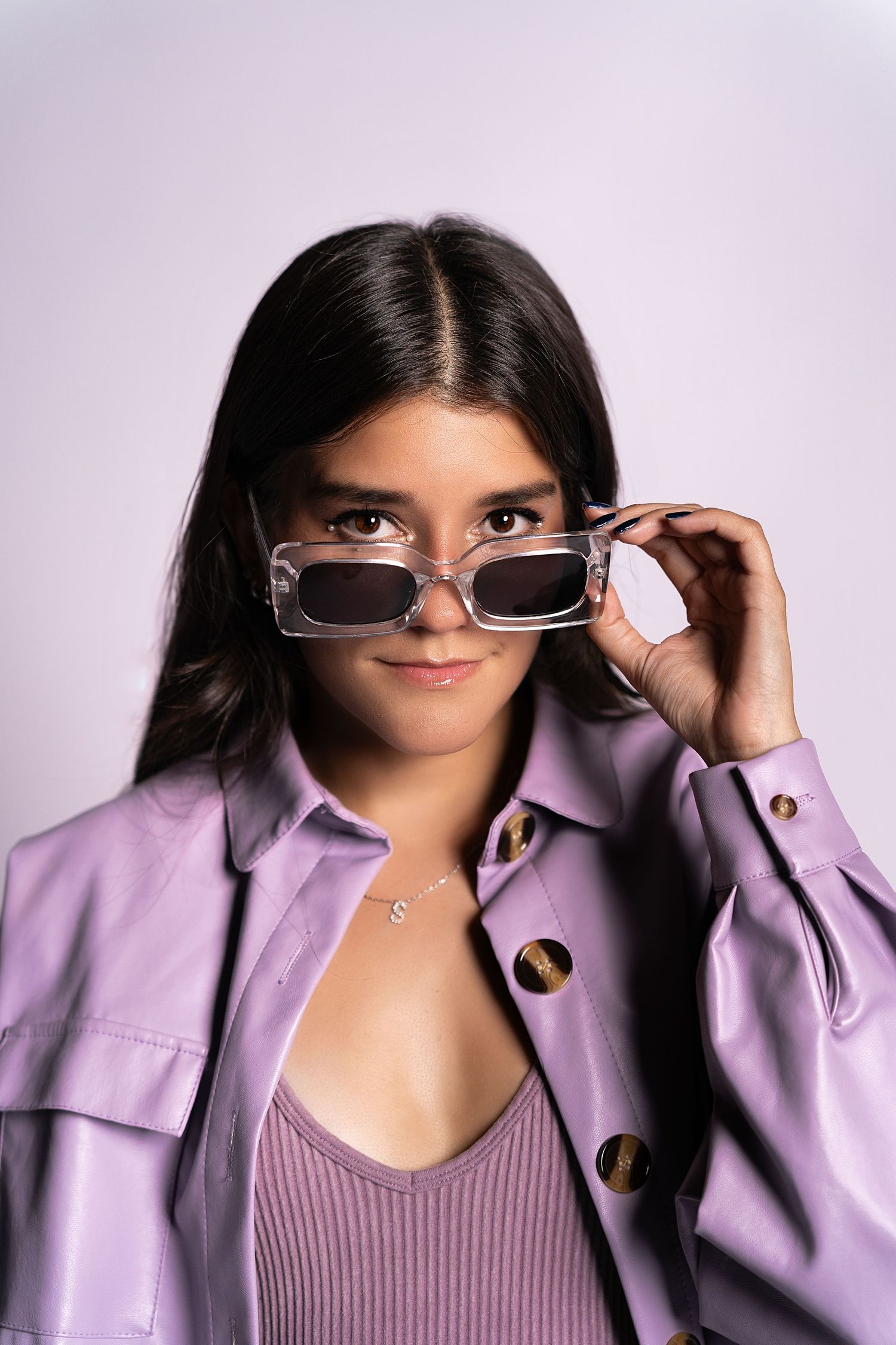 Sarah Sanchez. Sasainforma. Close-up fashion portrait featuring sunglasses and lavender jacket against light background.