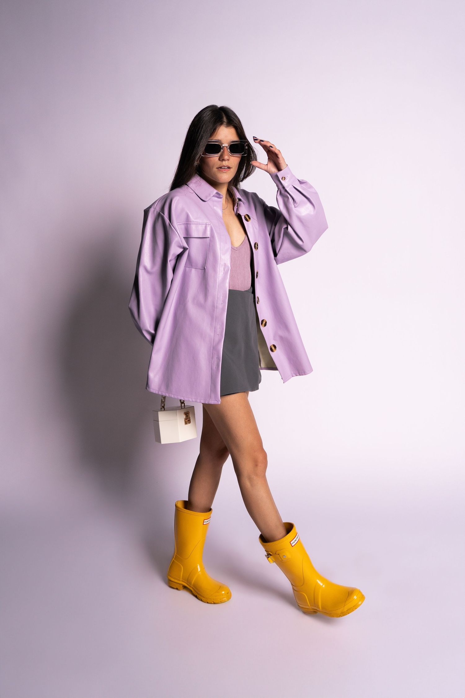 Sarah Sanchez. Sasainforma. Model strikes dynamic pose in lilac jacket and yellow rain boots against purple backdrop.