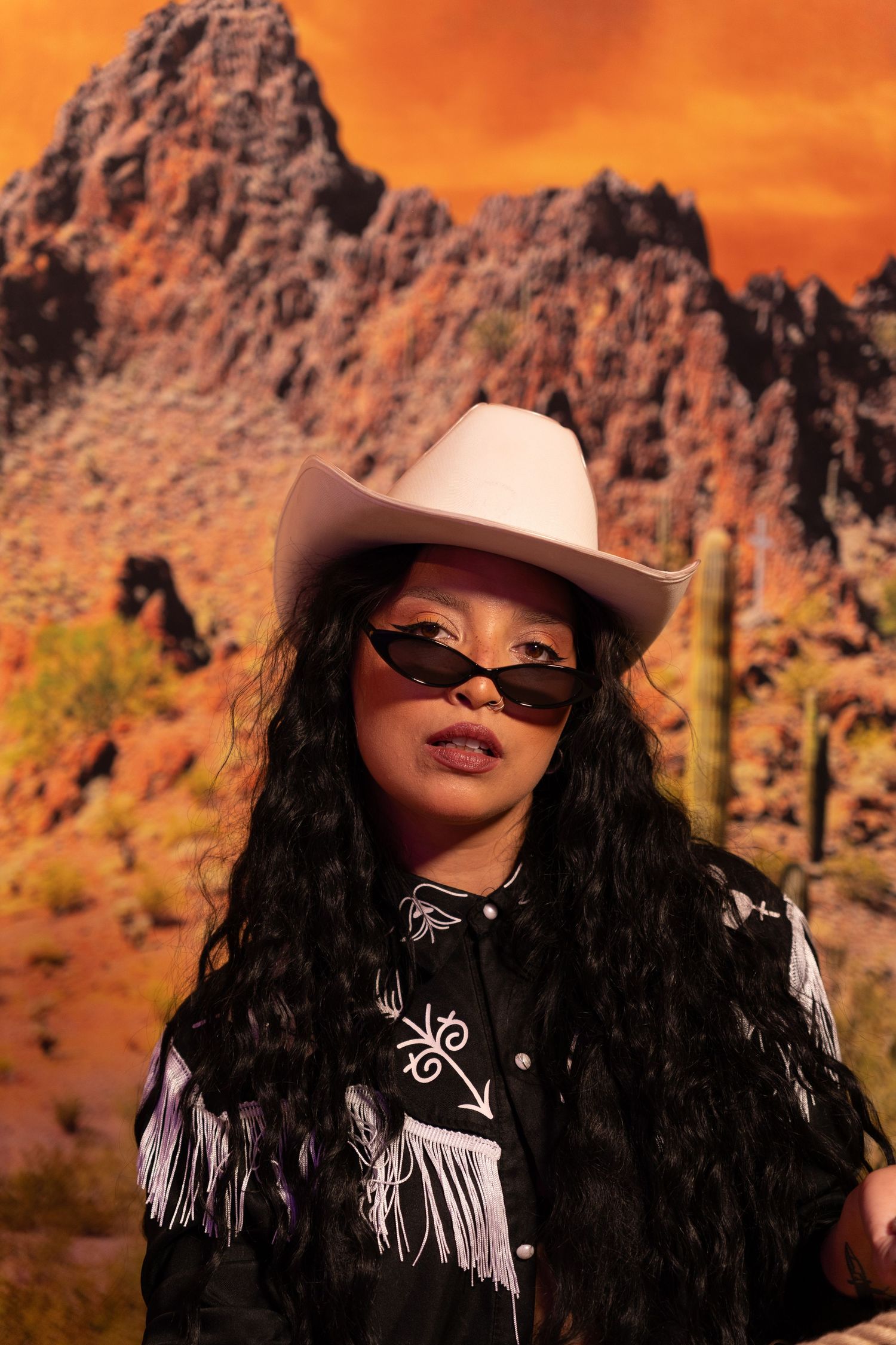 A western-styled portrait series against red desert rock formations features a figure in cowboy hat and fringe jacket.