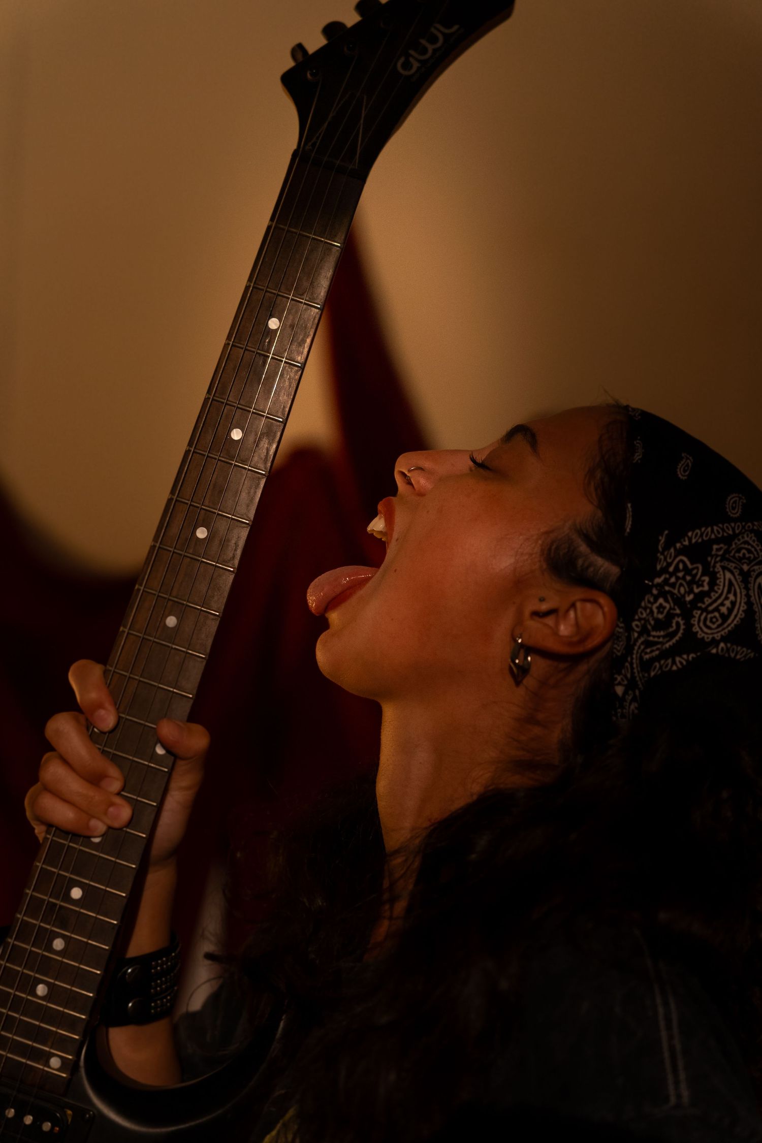 Musician sings passionately while playing electric guitar in moody brown lighting.