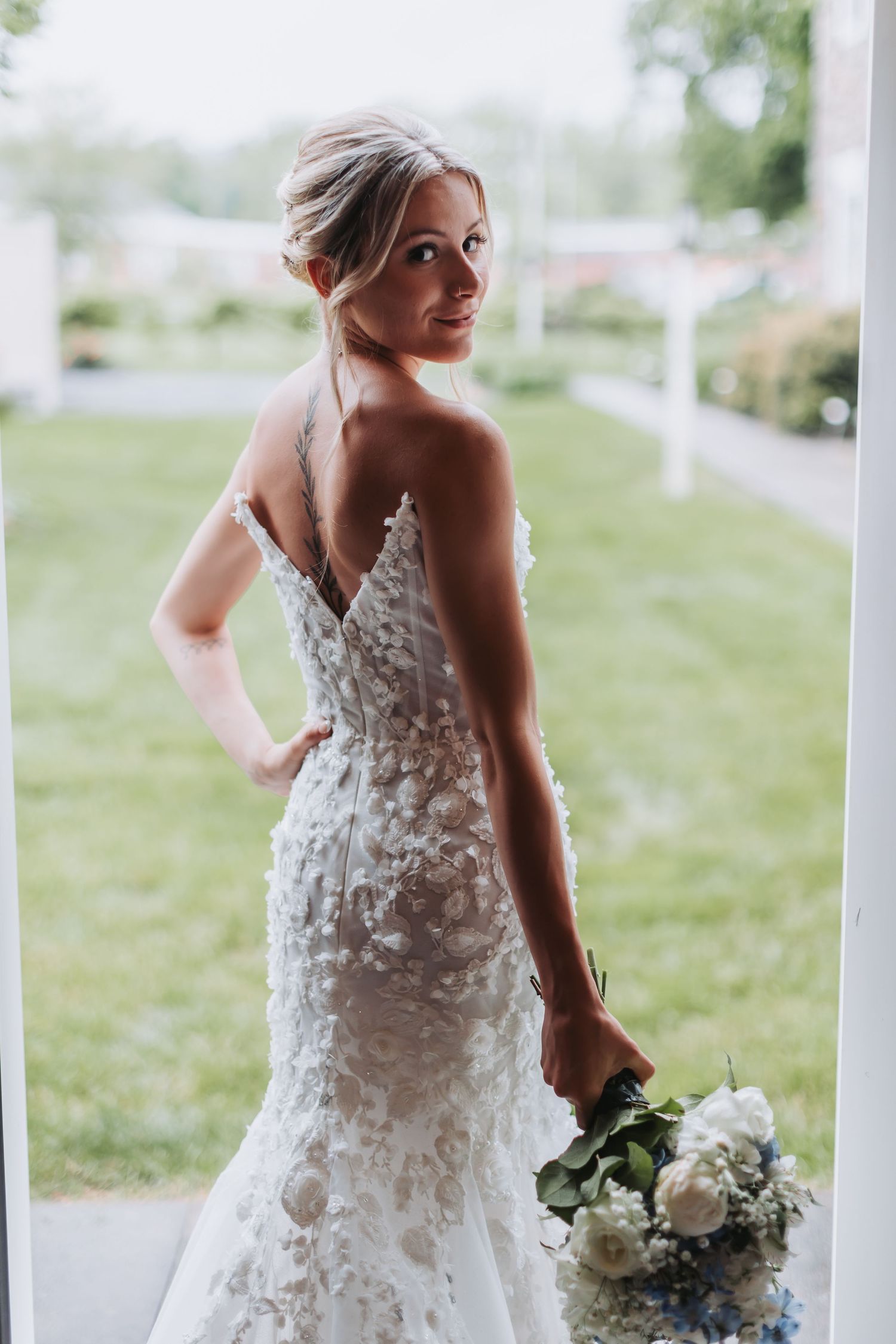 Back view of fitted lace wedding gown with delicate white bouquet.